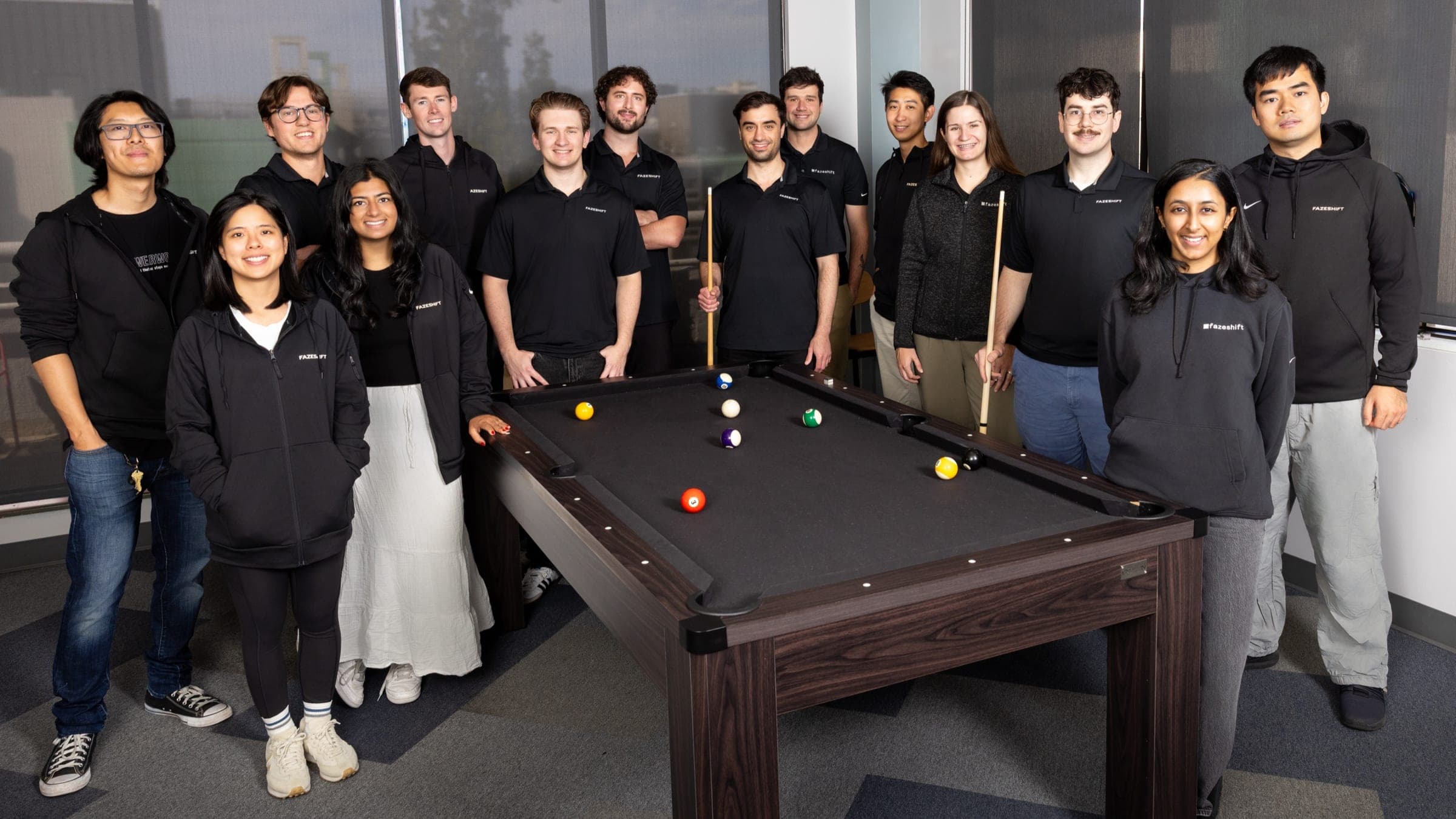 The Fazeshift team in branded jackets and polos around a pool table at the office