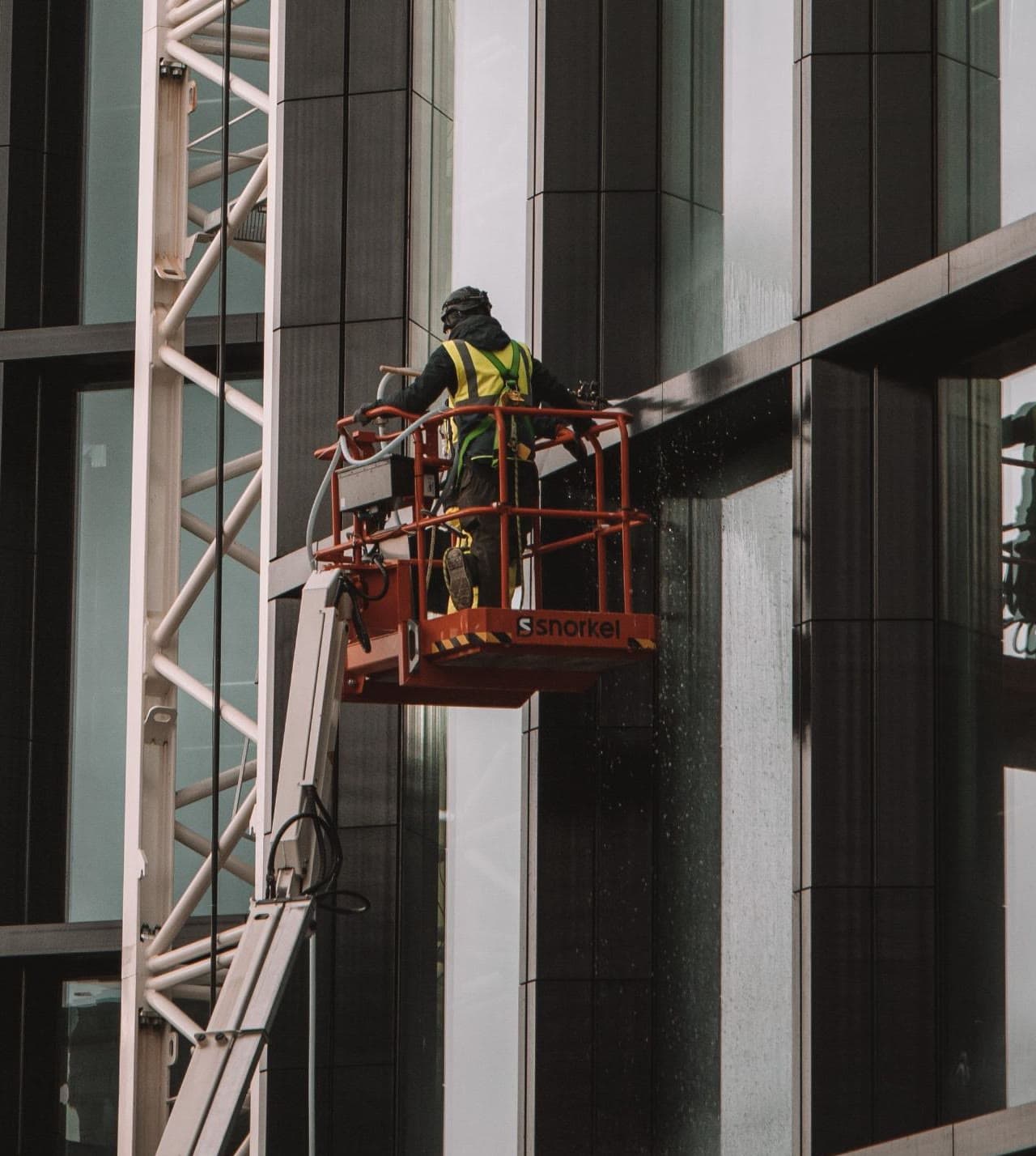 Worker on an aerial lift beside the glass facade of an office building