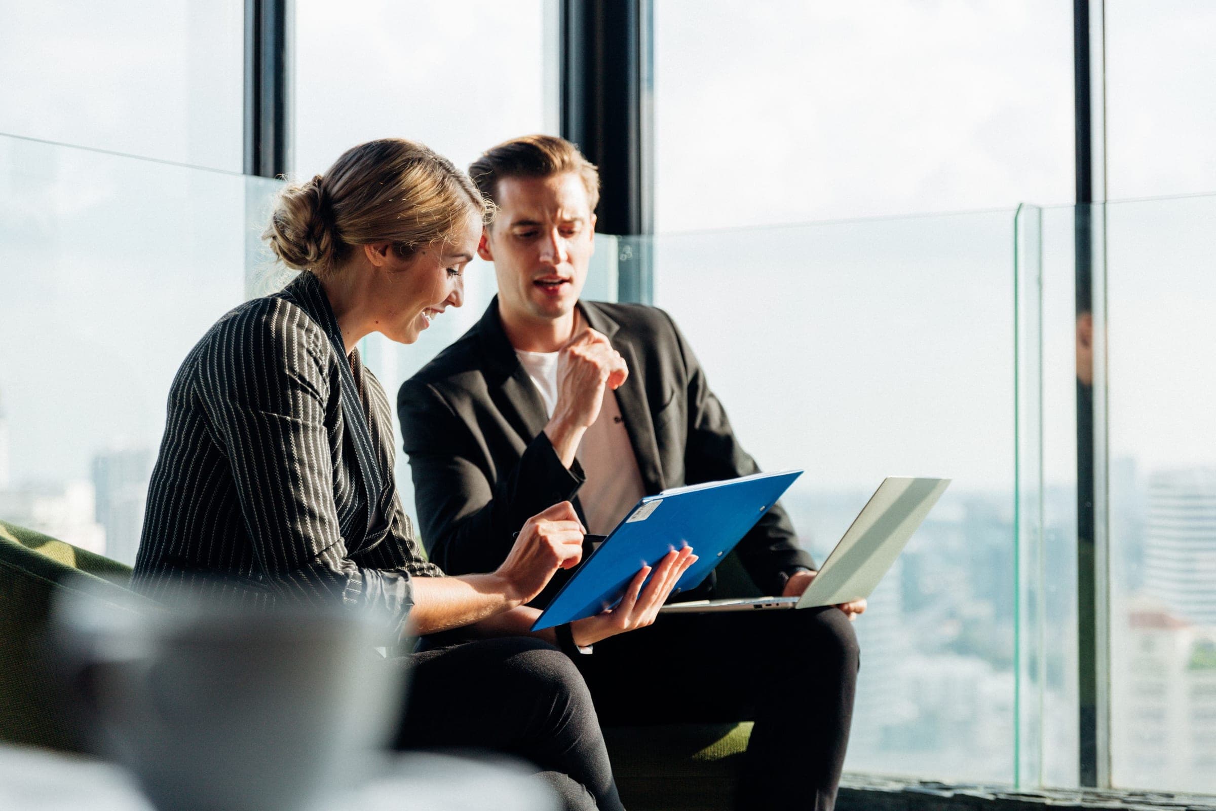 Two colleagues reviewing documents and a laptop in a high-rise office