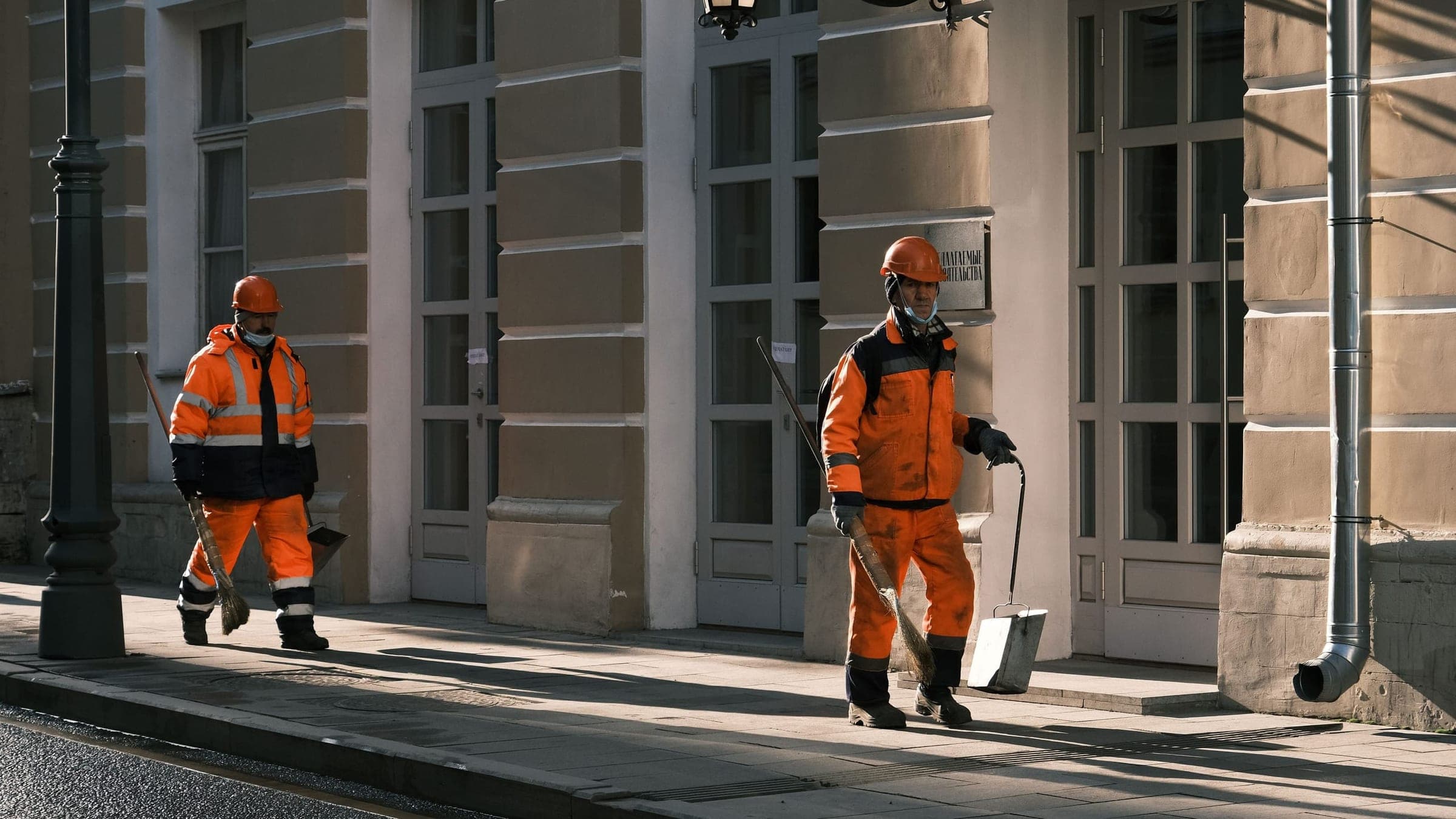 Two field technicians in orange high-visibility gear walking along a city street