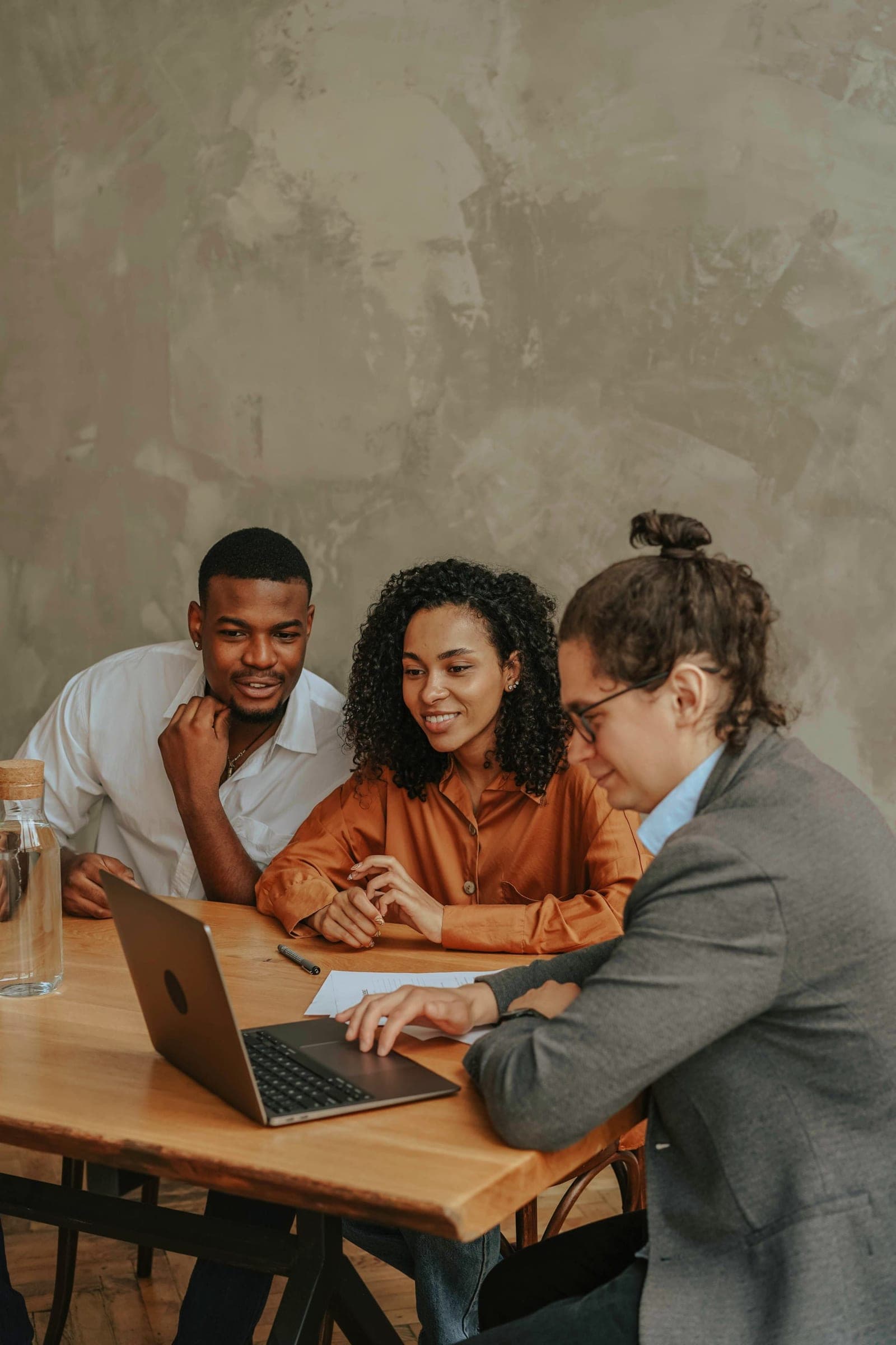 Three colleagues smiling as they review work together at a laptop